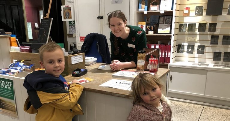 Two small children at the reception desk of the Royal Cornwall Museum with a smiling receptionist