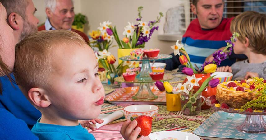Happy small boy eating a strawberry at a table in a Bosinver cottage with family