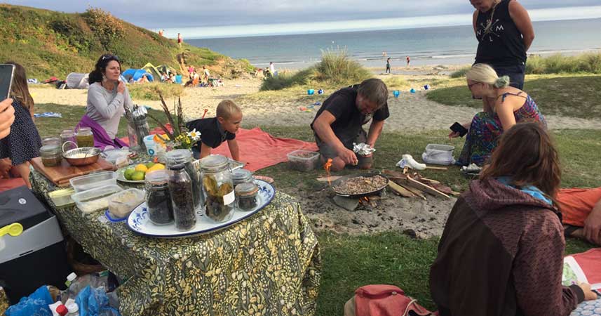 Family sat around a bbq on a Cornish beach cooking wild food with a table of ingredients.