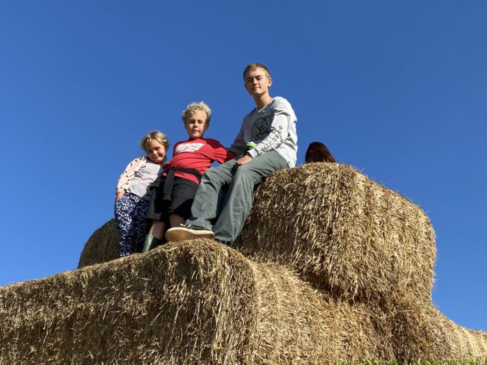 Pats three grandchildren sitting on top of a hay bale with a blue sky behind them