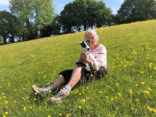 Nanny pat in a striped jumper sat in a field of buttercups, holding her dog