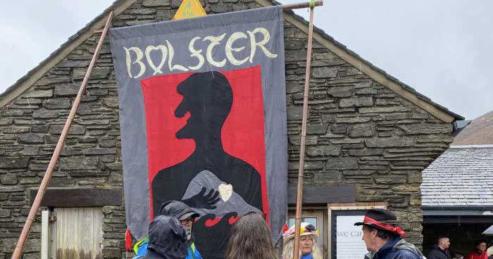 Several people hold a Bolster Pageant banner wearing traditional Cornish hat wear.
