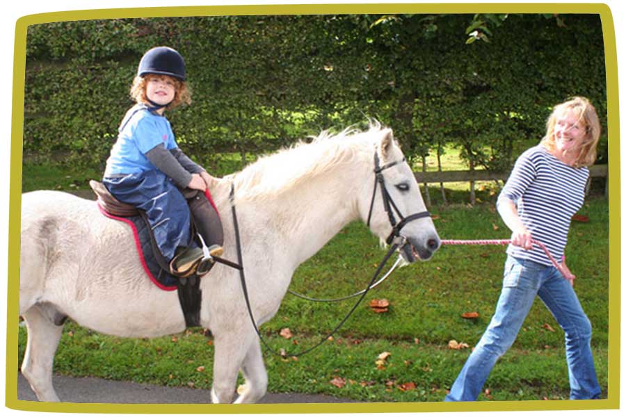 Young person riding a white whilst being led by an adult