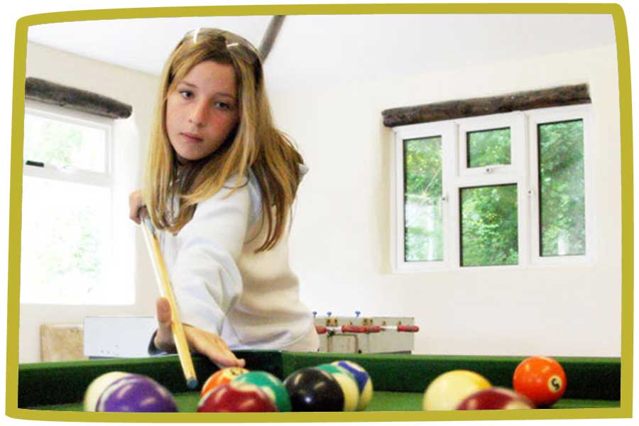 Close up of a girl playing pool in a white room with table football in the background