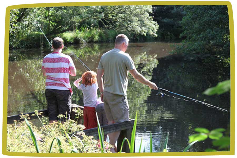 Three people fishing in a lake; two adults and a child. The sun is shining and reflecting off of the water