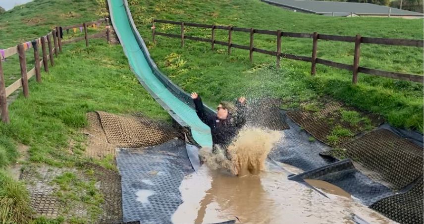A woman sliding down a large slide into a muddy pool of water in Cornwall