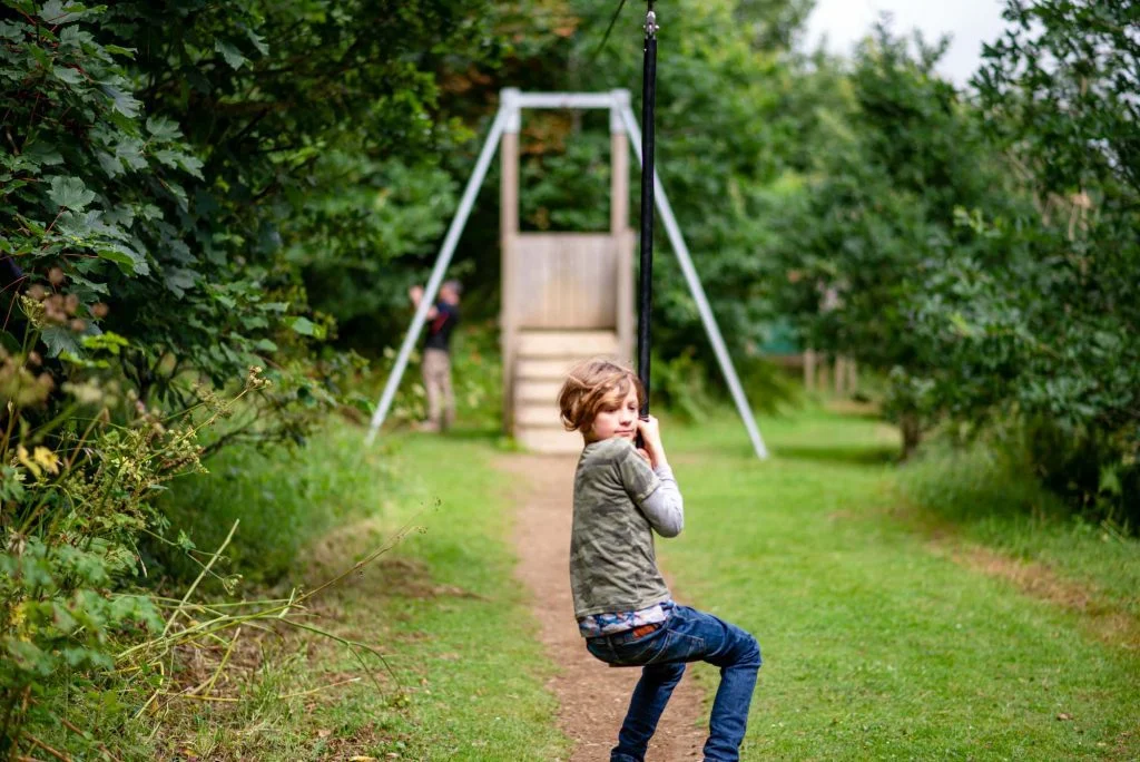 A blonde boy in jeans rides a zip wire
