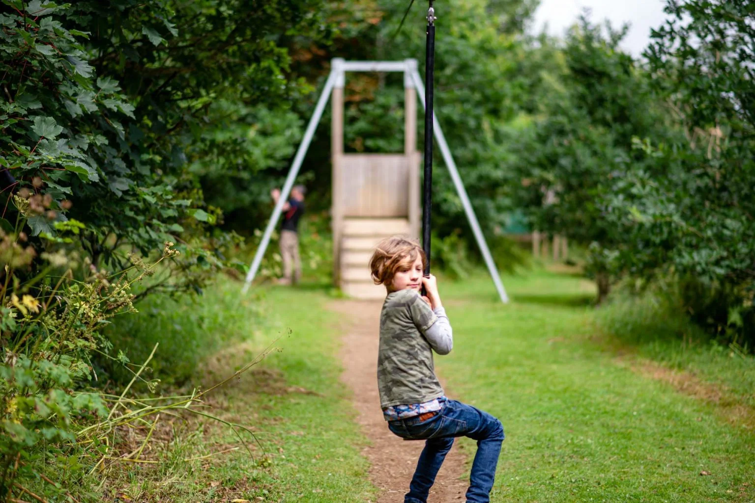 A blonde boy in jeans rides a zip wire