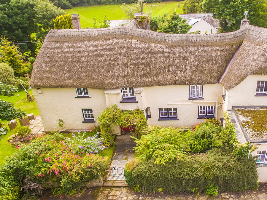 Aerial shot of a traditional thatched Cornish farmhouse with traditional windows and a red front door