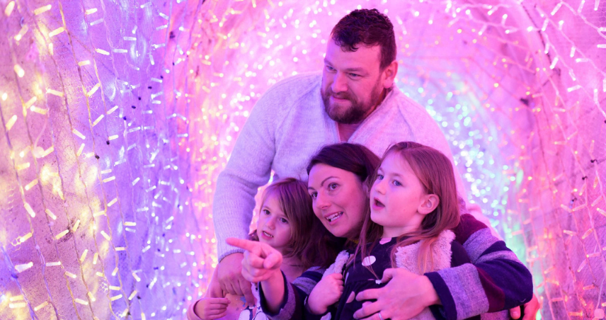 Family looking at the purple lights together that are hung up around a large tunnel.