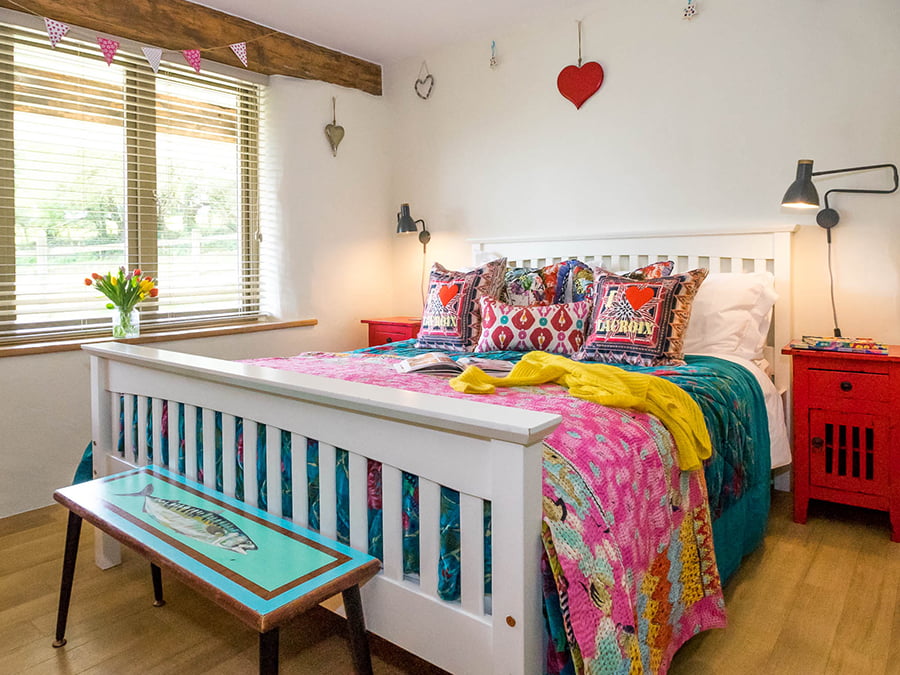 A white framed bed with brightly coloured bedding and red bedside tables.
