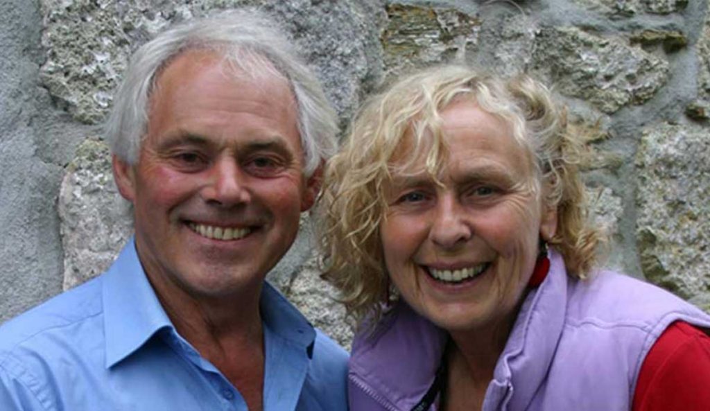 A smiling couple in front of a stone wall looks towards the camera