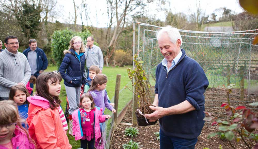 Man showing a group of children and adults a plant being grown in a vegetable garden