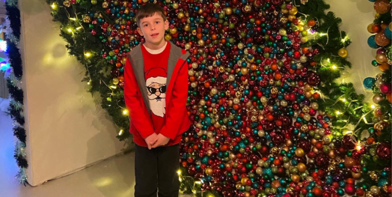 Boy standing in front of a wall of Christmas baubles in Cornwall.