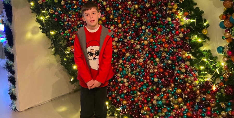 Boy standing in front of a wall of Christmas baubles in Cornwall.