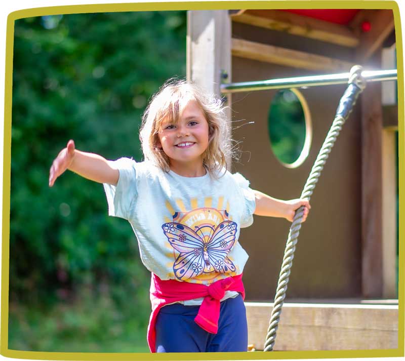 Child smiling and playing on a climbing frame outside at Bosinver.