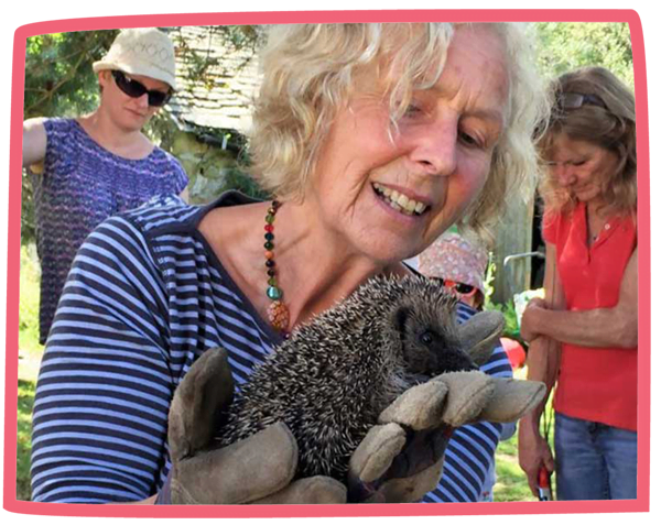 Nanny Pat wearing gloves and holding a hedgehog with several adults in the background.