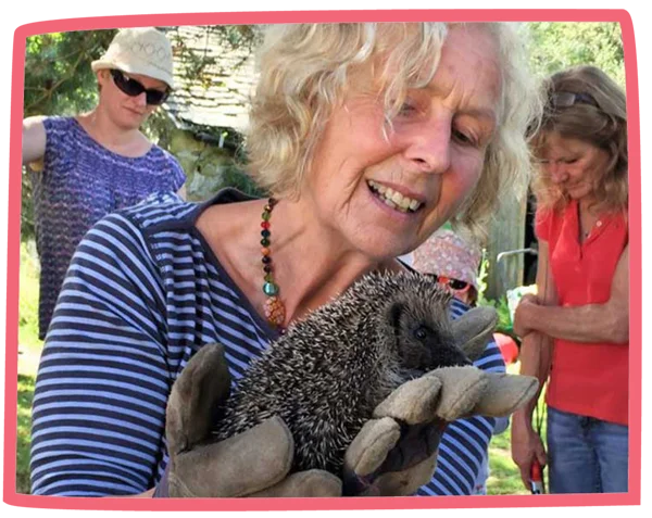 Nanny Pat wearing gloves and holding a hedgehog with several adults in the background.