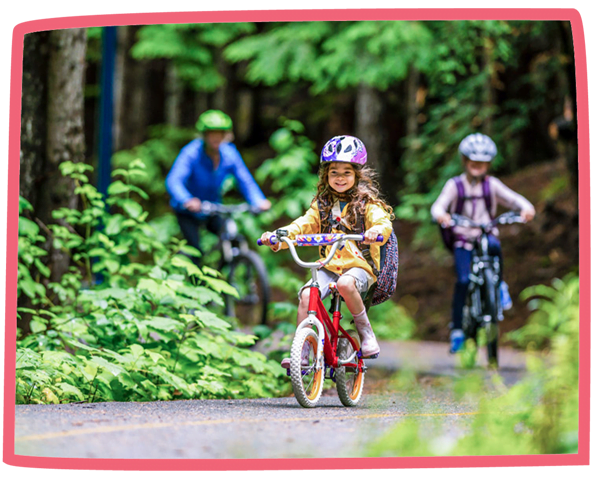 Close up of a child riding a bike in a woodland, with the rest of the family cycling behind them.