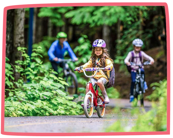 Close up of a child riding a bike in a woodland, with the rest of the family cycling behind them.