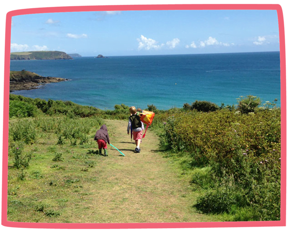 Two children walking towards the coast with a kite in Cornwall on a sunny day.