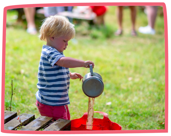 Child pouring mud from a saucepan into a bucket whilst playing in the mud kitchen at Bosinver.
