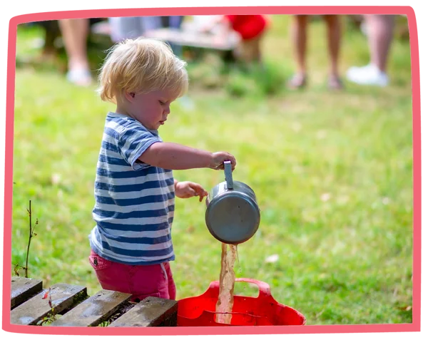 Child pouring mud from a saucepan into a bucket whilst playing in the mud kitchen at Bosinver.