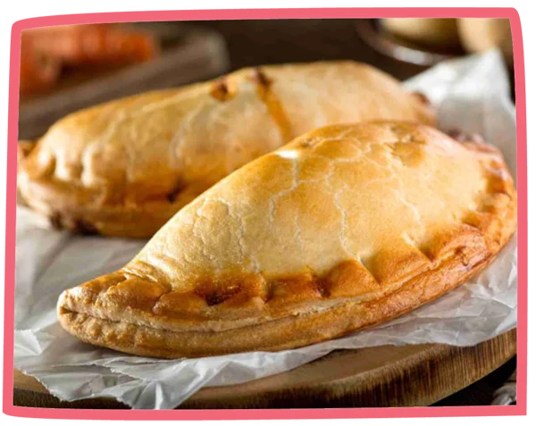 Two fresh pasties fresh out of the oven on grease proof paper.