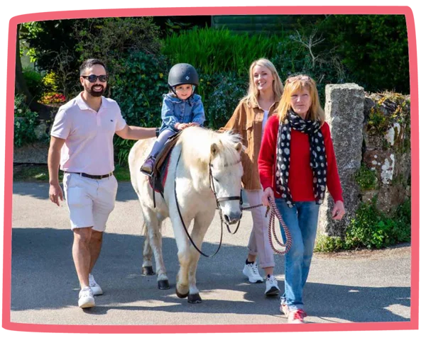 Small child riding a pony at Bosinver on a sunny day with adults supervising.