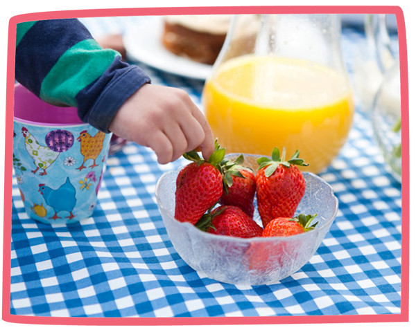 Small child taking strawberries from a bowl that also has a jug of orange juice.