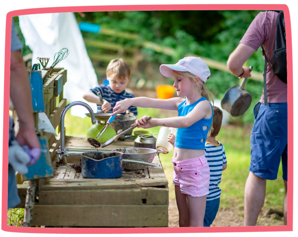 Group of three children using a mud kitchen at Bosinver whilst adults look on.