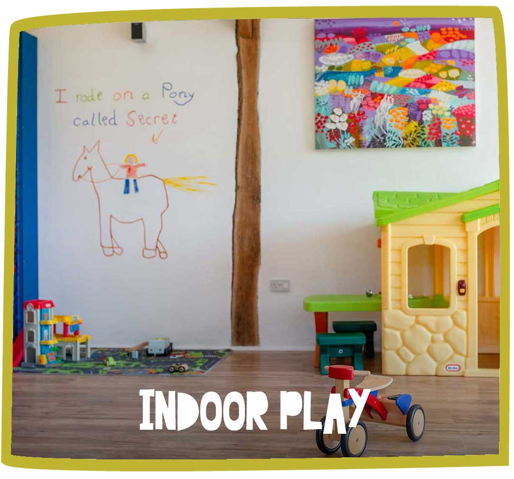 Indoor play area at Bosinver, including a tricycle, play house and a drawing of a pony.
