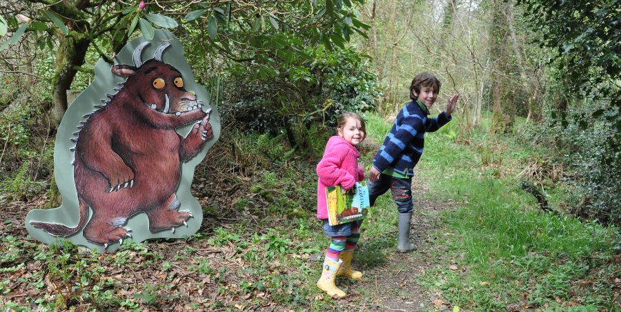 Boy and girl holiding The Gruffalo Book in woodland standing next to large Gruffalo cut out. 