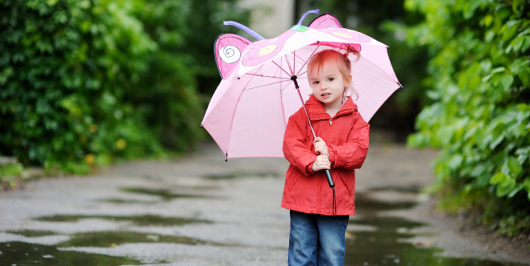 Small child standing in lane with puddles of water holding umbrella