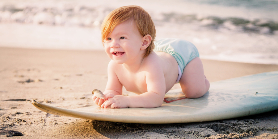 Baby knelt down on a surf board on the shore line