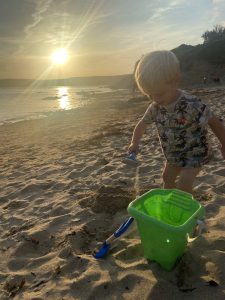 Toddler playing in the sand on the beach as the sunsets over the sea in the background