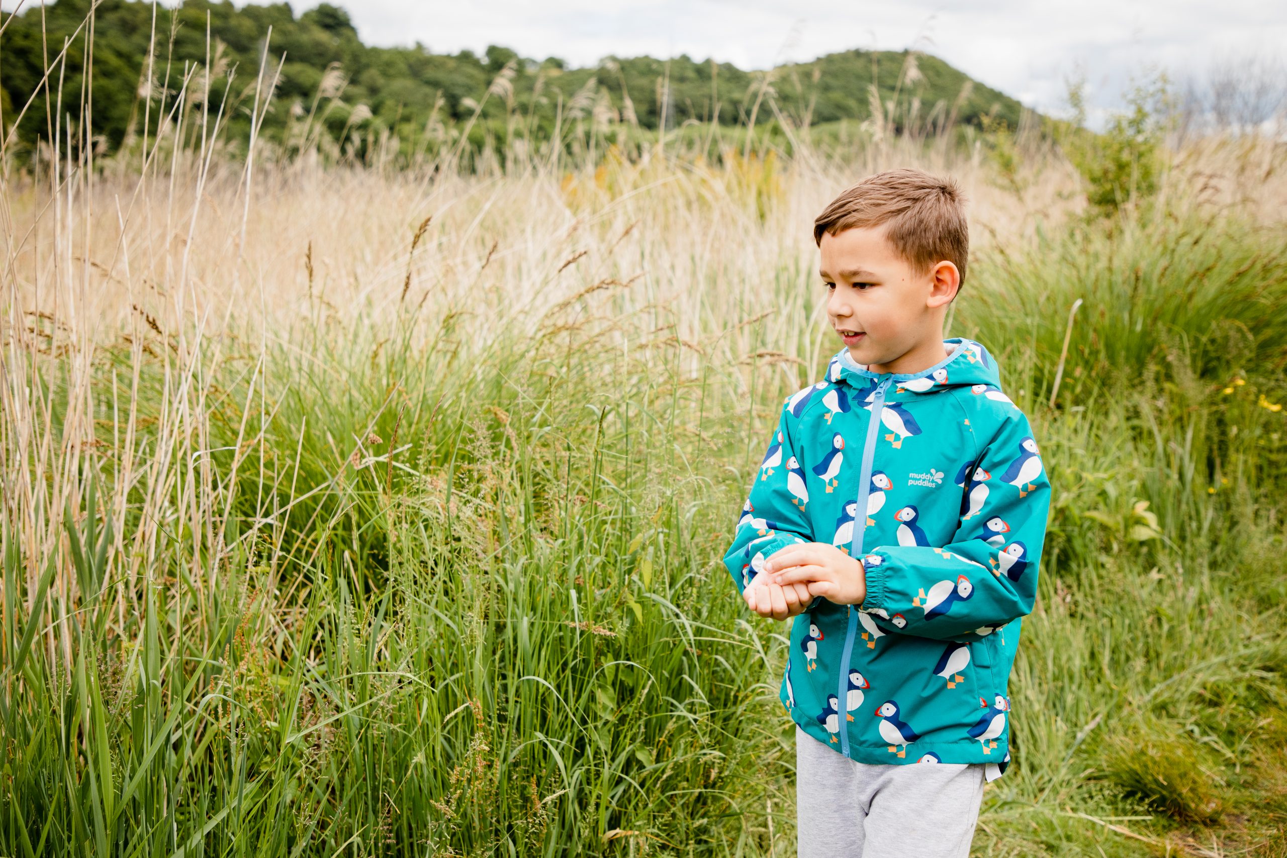 Boy in a colourful coat amogst long grass near coast