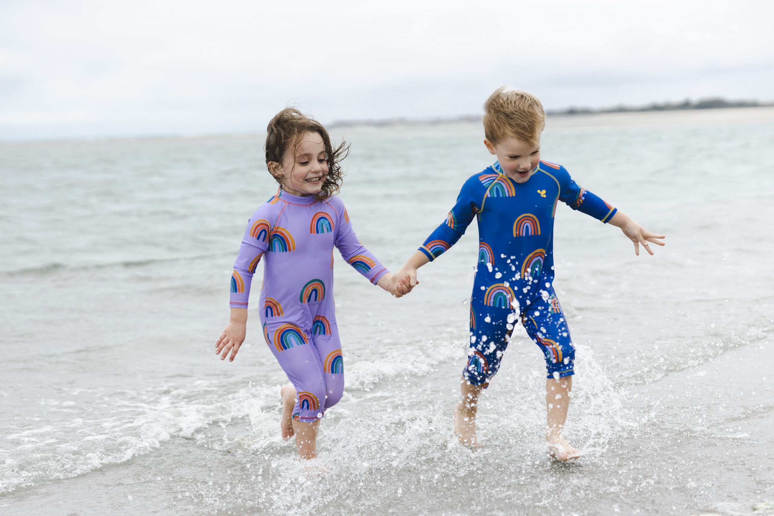 2 young children running through shallow sea water on a beach