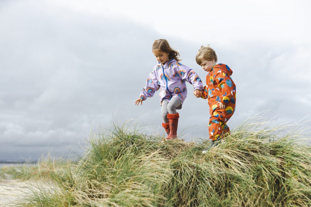 two childen on top of sand dunes in bright coloured outer wear.