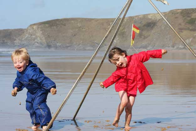 2 children on the beach with wet weather gear on