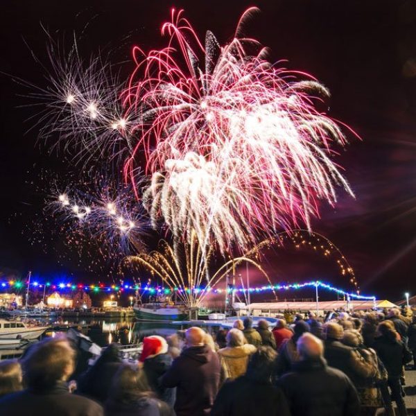 Fireworks over a harbour in Cornwall with a large crowd watching.