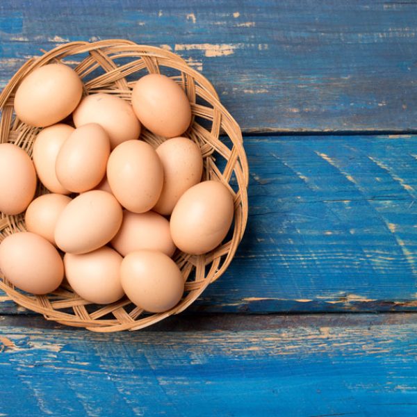 Close up of eggs in a basket on a blue table.